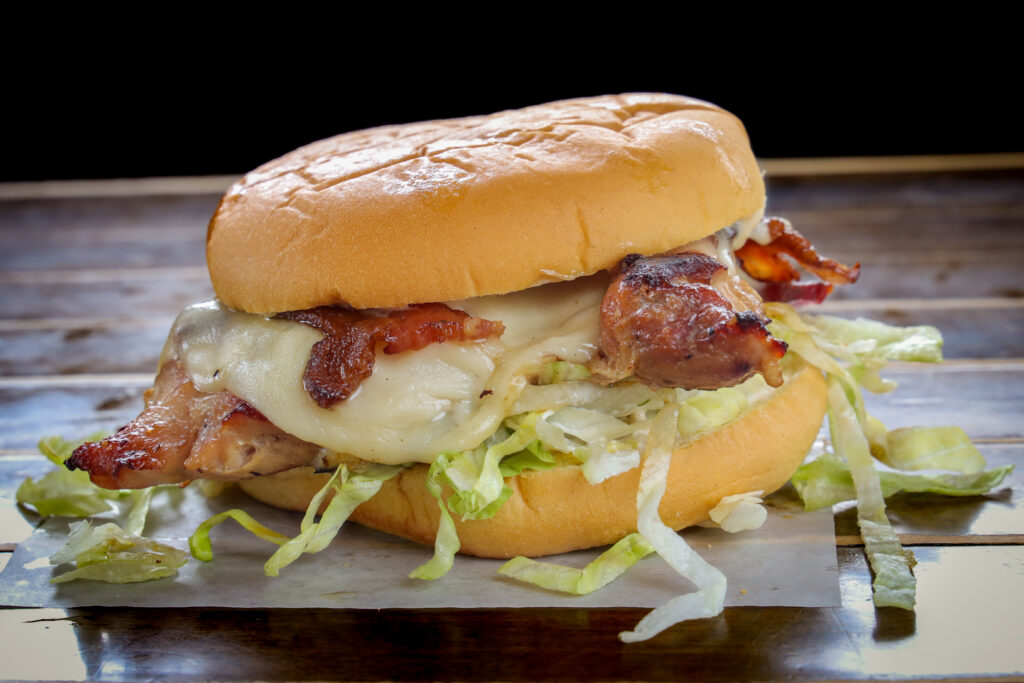 Grilled chicken sandwich with bacon, melted white cheese, and shredded lettuce on a potato roll