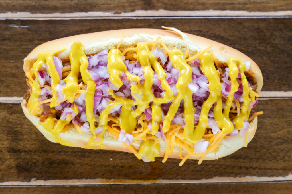 Classic Coney chili cheese hot dog topped with shredded cheddar, diced red onion, and yellow mustard