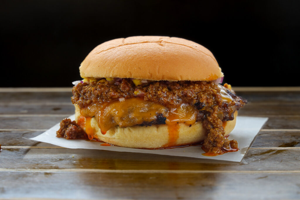 Smash burger with melted cheddar cheese and beef chili topping, sauce dripping onto a soft bun