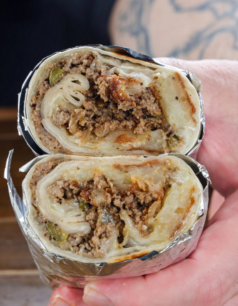 Beef picadillo burrito with grilled onions, hatch green chile, latkes, and queso sliced open, close-up view