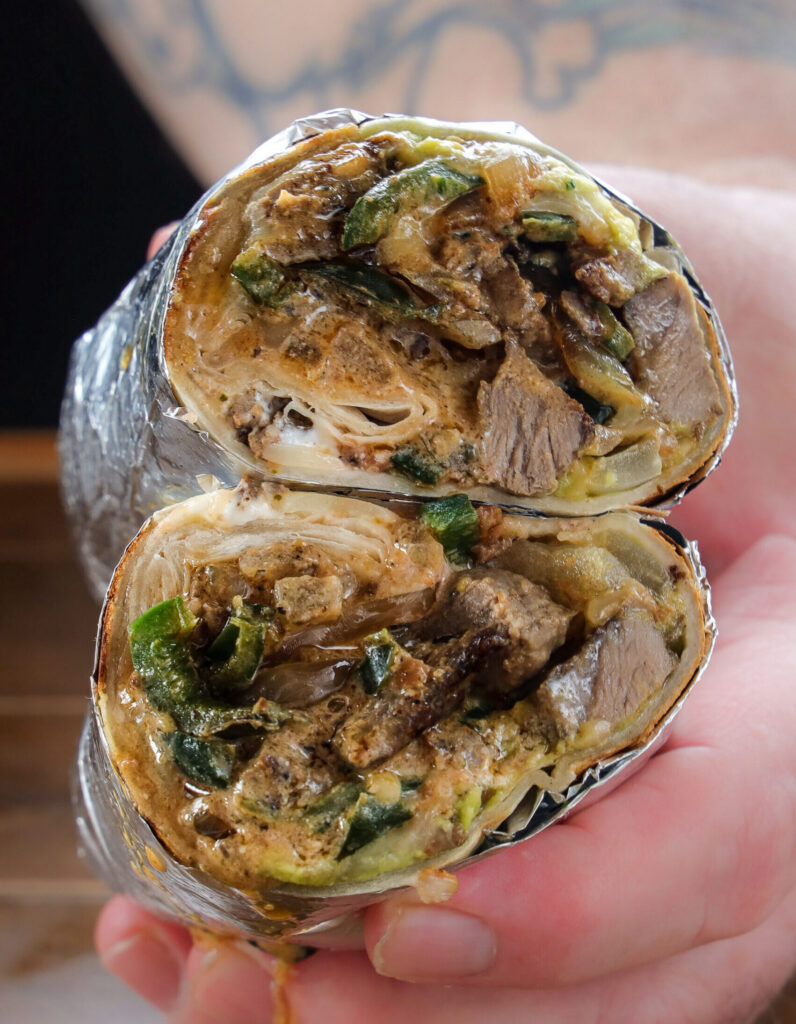 Carne asada burrito with grilled steak, poblano peppers, guacamole, sour cream, and melted cheese sliced in half