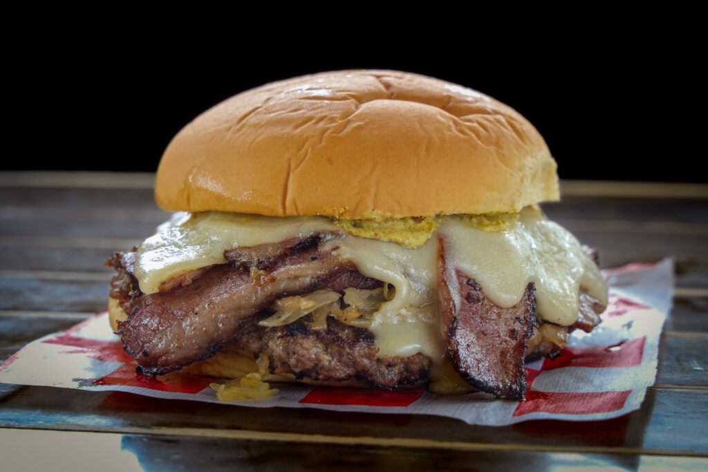 Smashed burger topped with pastrami, melted swiss cheese, pickles, and mustard on a toasted bun