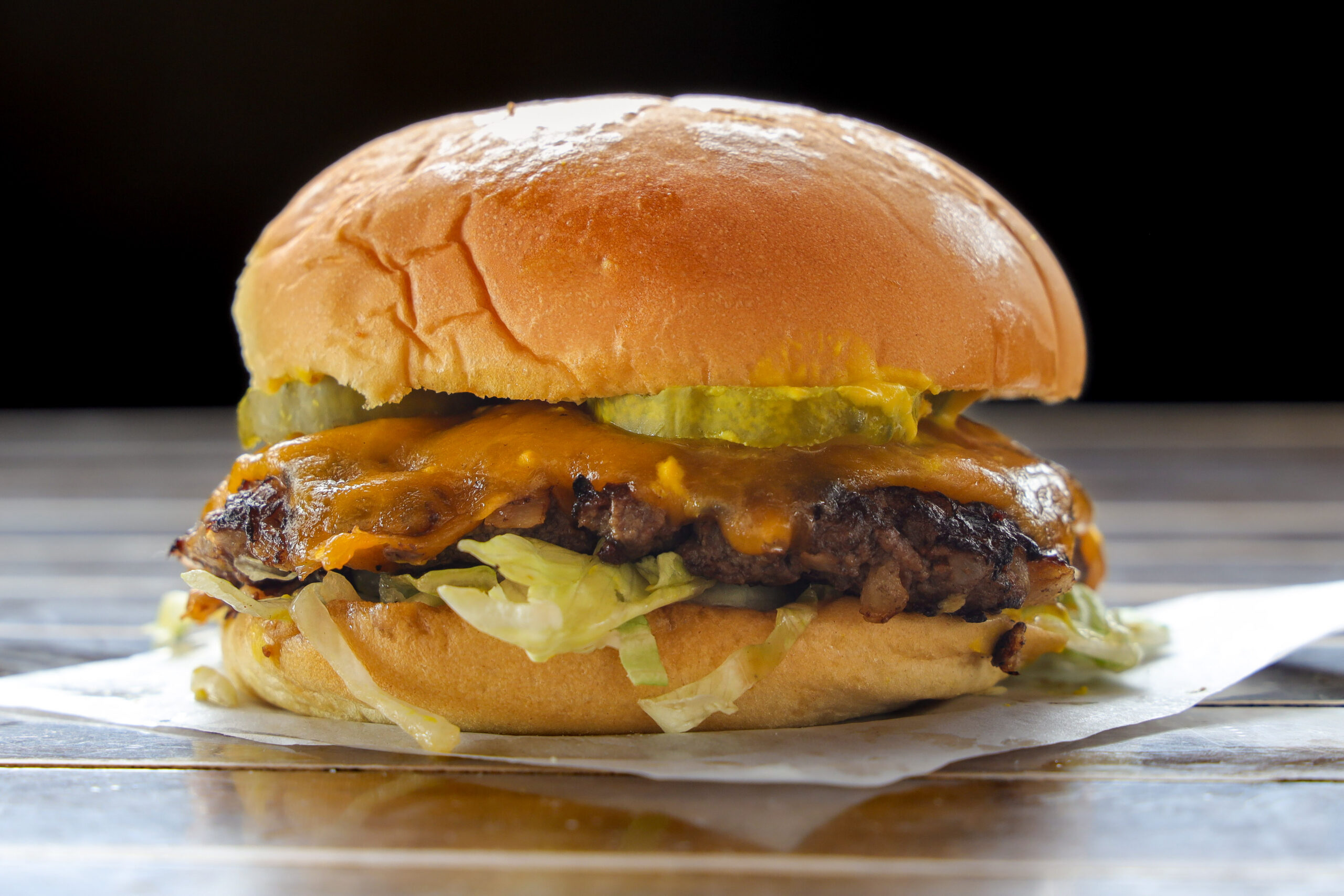 Juicy cheeseburger with melted cheddar cheese, pickles, and lettuce on a soft bun, placed on a wooden surface.