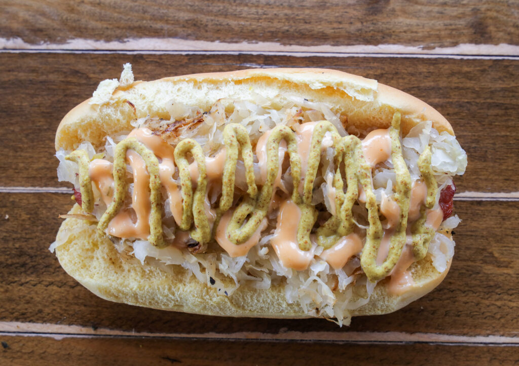 Sauerkraut hot dog topped with brown mustard and 1000 island dressing drizzle