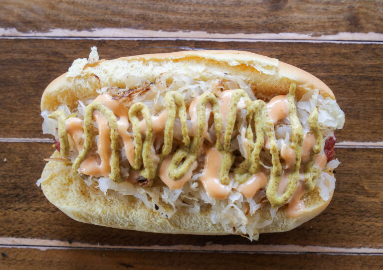 Sauerkraut hot dog topped with brown mustard and 1000 island dressing drizzle