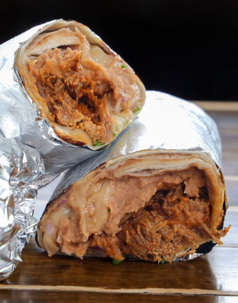 Barbacoa beef burrito with refried beans sliced in half, wrapped in foil, showing shredded meat and bean filling