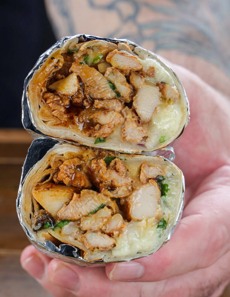 Grilled chicken burrito with melted cheese and mexican rice sliced in half, held up close-up in hand
