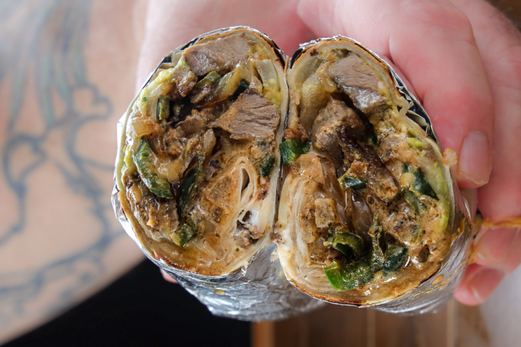 Carne asada burrito with grilled steak, poblano peppers, guacamole, sour cream, and melted cheese sliced in half